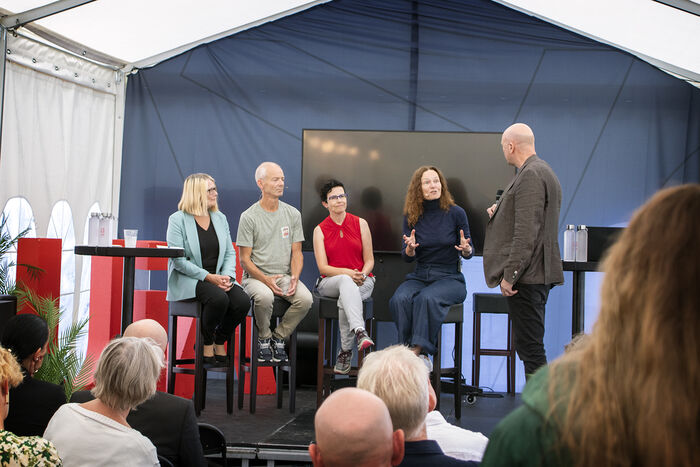 Bildet viser folk som diskuterer på scene inne i telt
