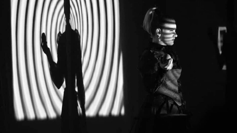 A dancer stands in front of a projector that projects a circle pattern in black and white