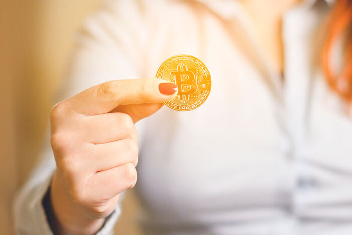 Illustrasjonsbilde, kvinne holder fram en gullmynt med logoen til kryptovalutaen Bitcoin