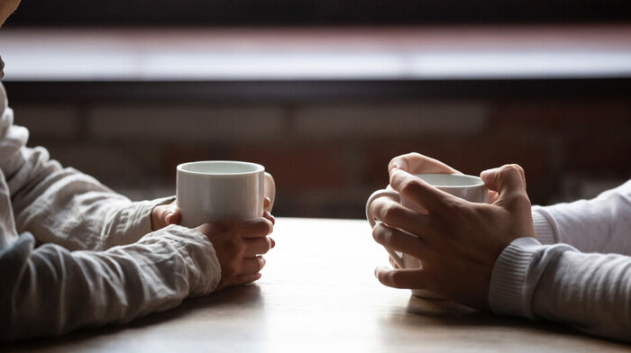 Image of two persons with coffee cups having a conversation.