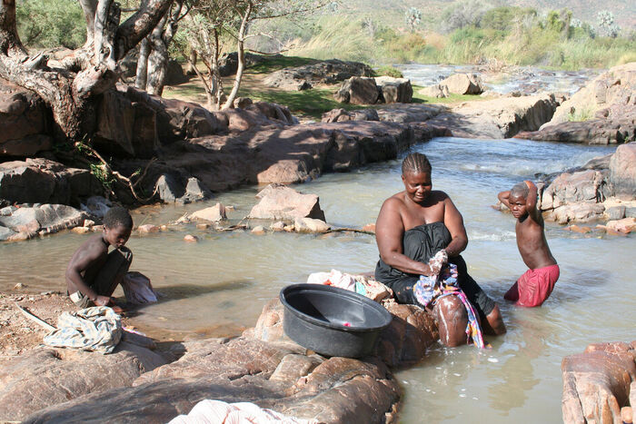 Bildet viser kvinne som vasker klær i elva. 