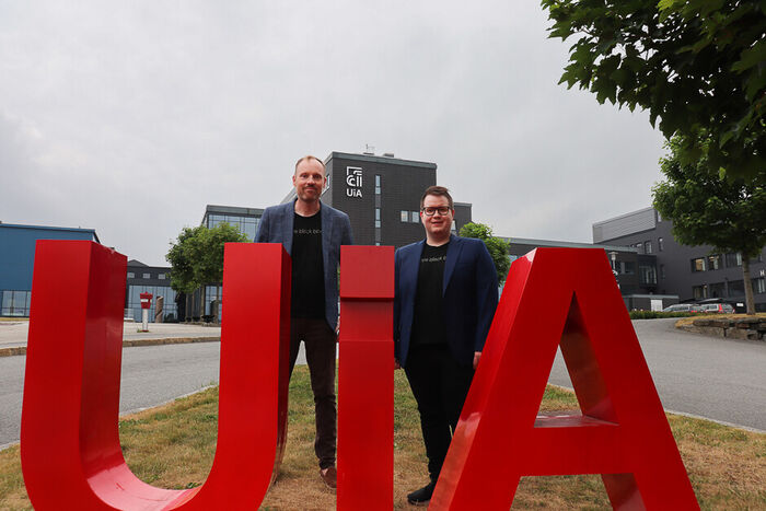 Photo of the researchers in front of the UiA logo on the lawn on Campus Grimstad