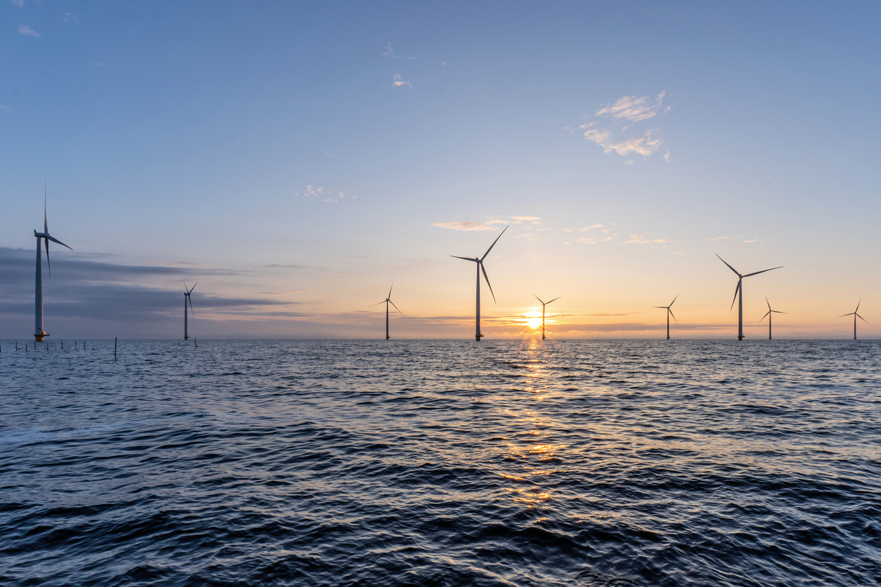 photography of offshore windmills at sunset