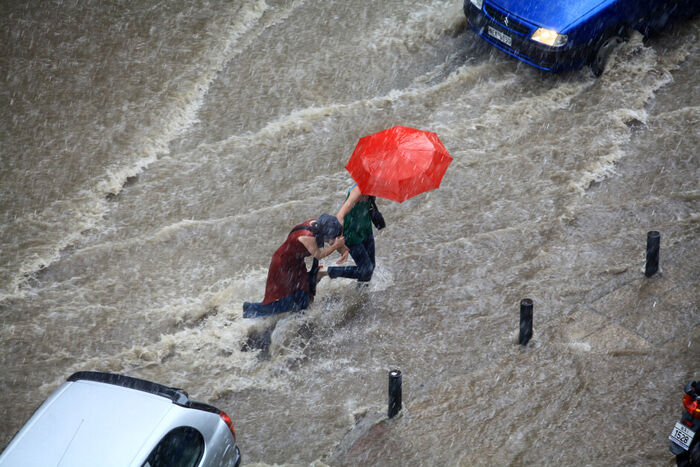 Oversvømt vei, uvær, folk under rød paraply