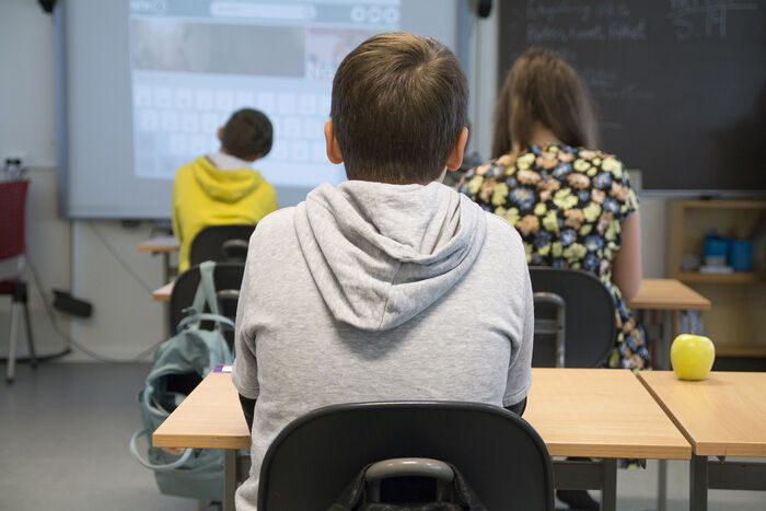 Bildet viser ryggen til en elev som sitter ved en pult i et klasserom.