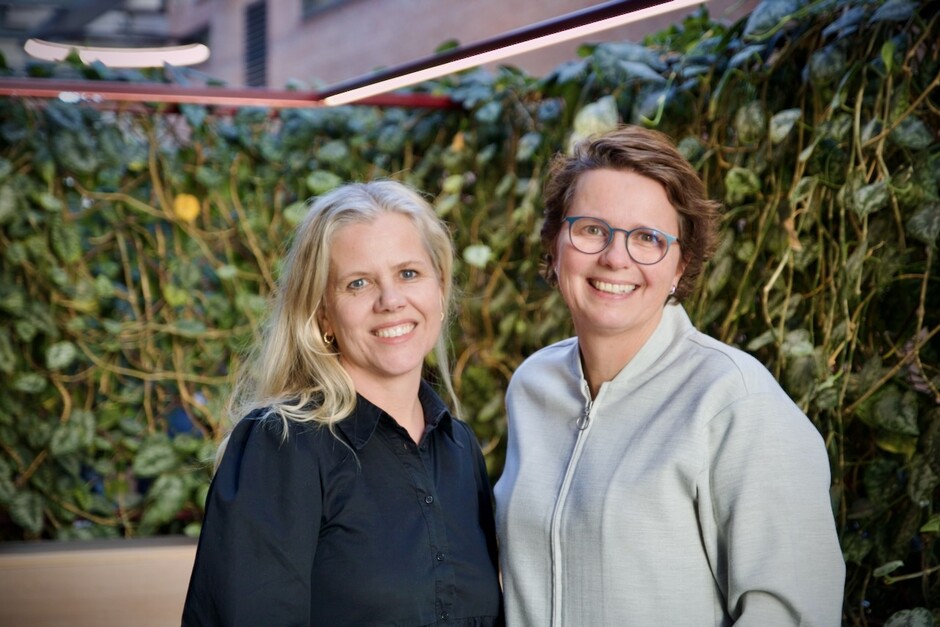 Vigdis Guttormsen og Margrethe Røed smiler foran plantevegg i Vrimlehallen, K