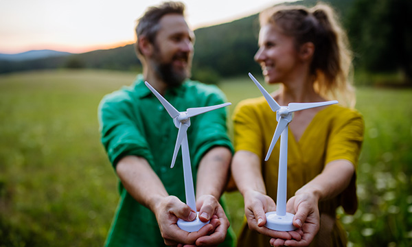 Two people in a green field holding models of wind mills, smiling