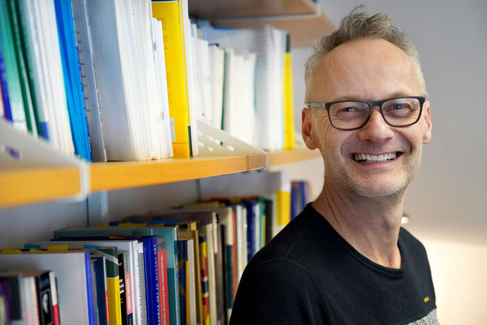 Professor i statsvitenskap, Jarle Trondal, står foran en bokhylle og smiler.