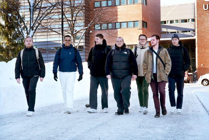 Syv mannlige sosionomstudenter spaserer nedover veien foran hovedinngangen til Universitetet i Agder