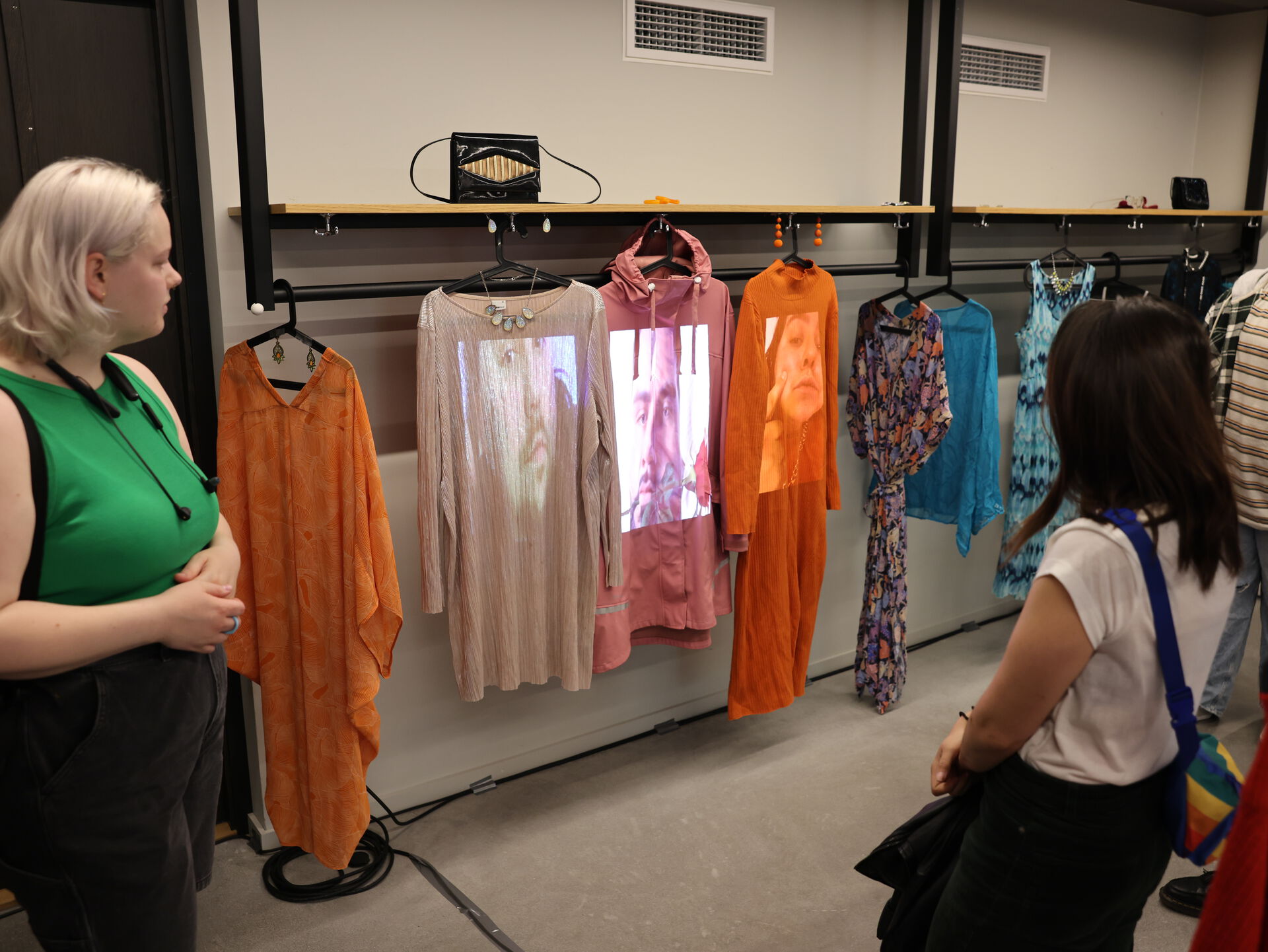 Bildet viser flere kjoler hengende i en garderobe. En prosjektor viser levende bilder av ansikter på kjolene, som dermed fungerer som et slags lerret.