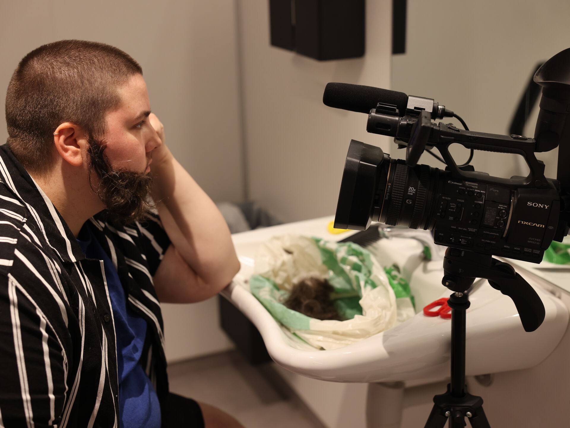 Bildet viser kunstneren RAVN, som har limt på seg et mørkt skjegg.  filmes i det han barberer seg.