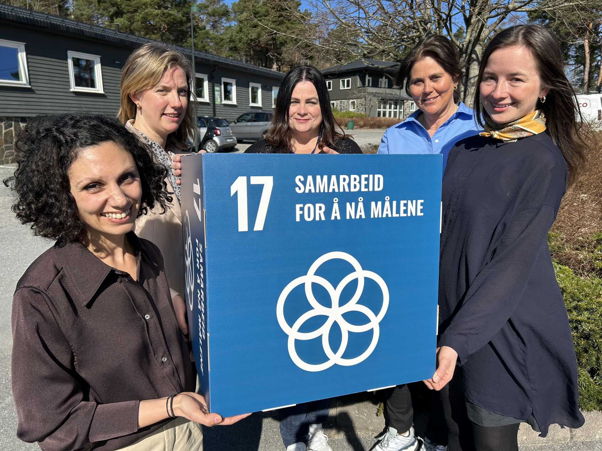 De fire personene på bildet holder frem en boks med FNs bærekraftmål nummer 17: Samarbeid for å nå målene.