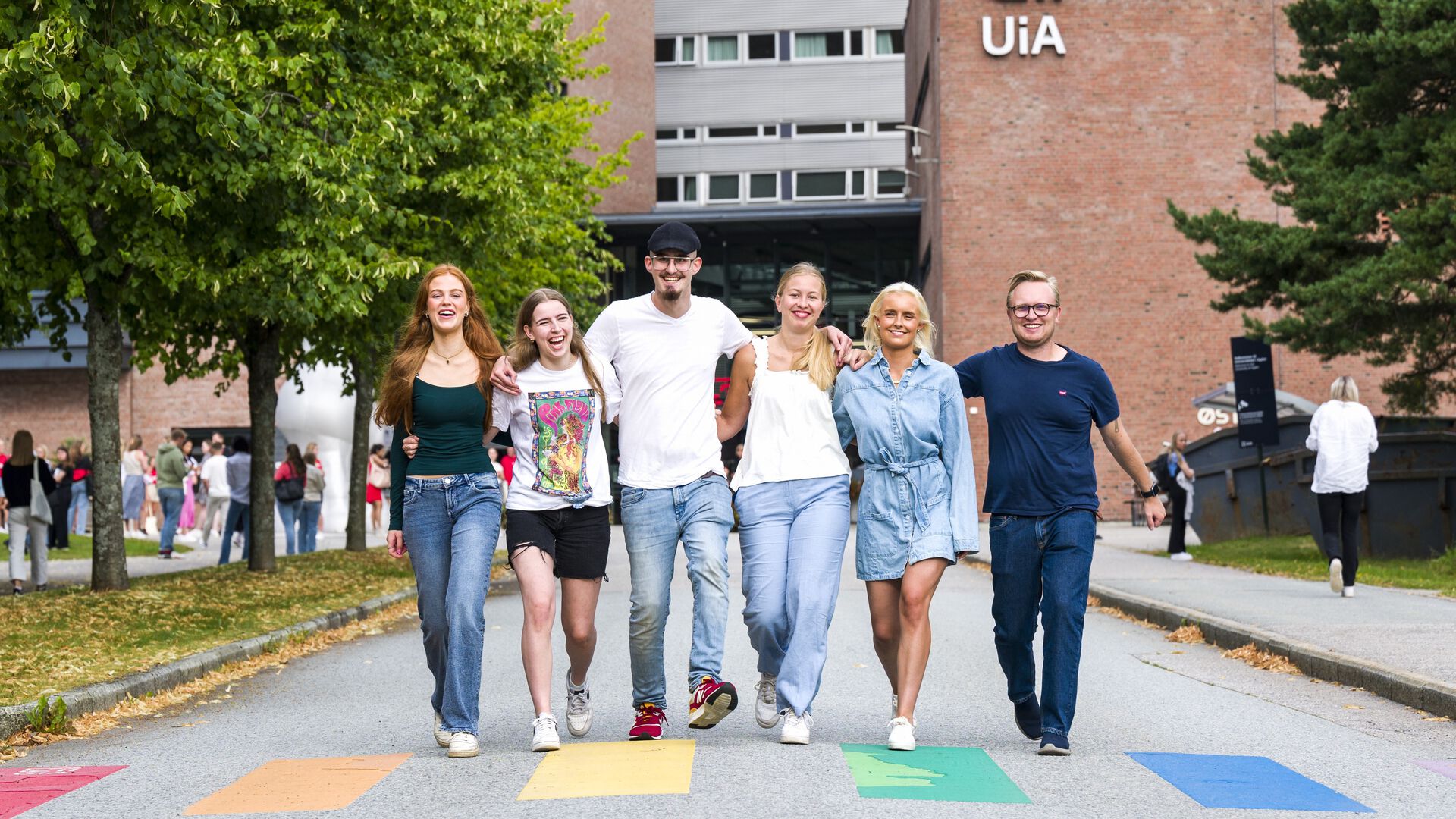 Fem studenter foran hovedinnganga til UiA i Kristiansand, ved et regnbue-gangfelt