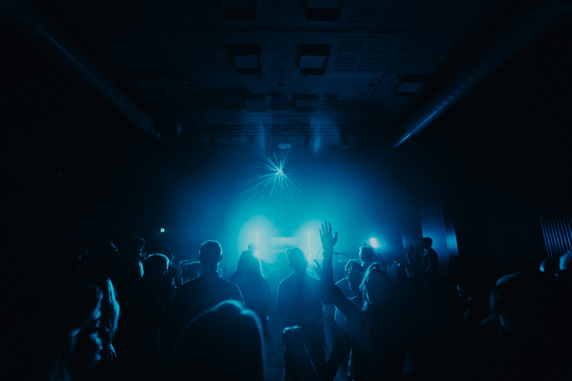 Mørkt konsertlokale, røyk og lys i blå farge, et stort publikum som holder hendene i været