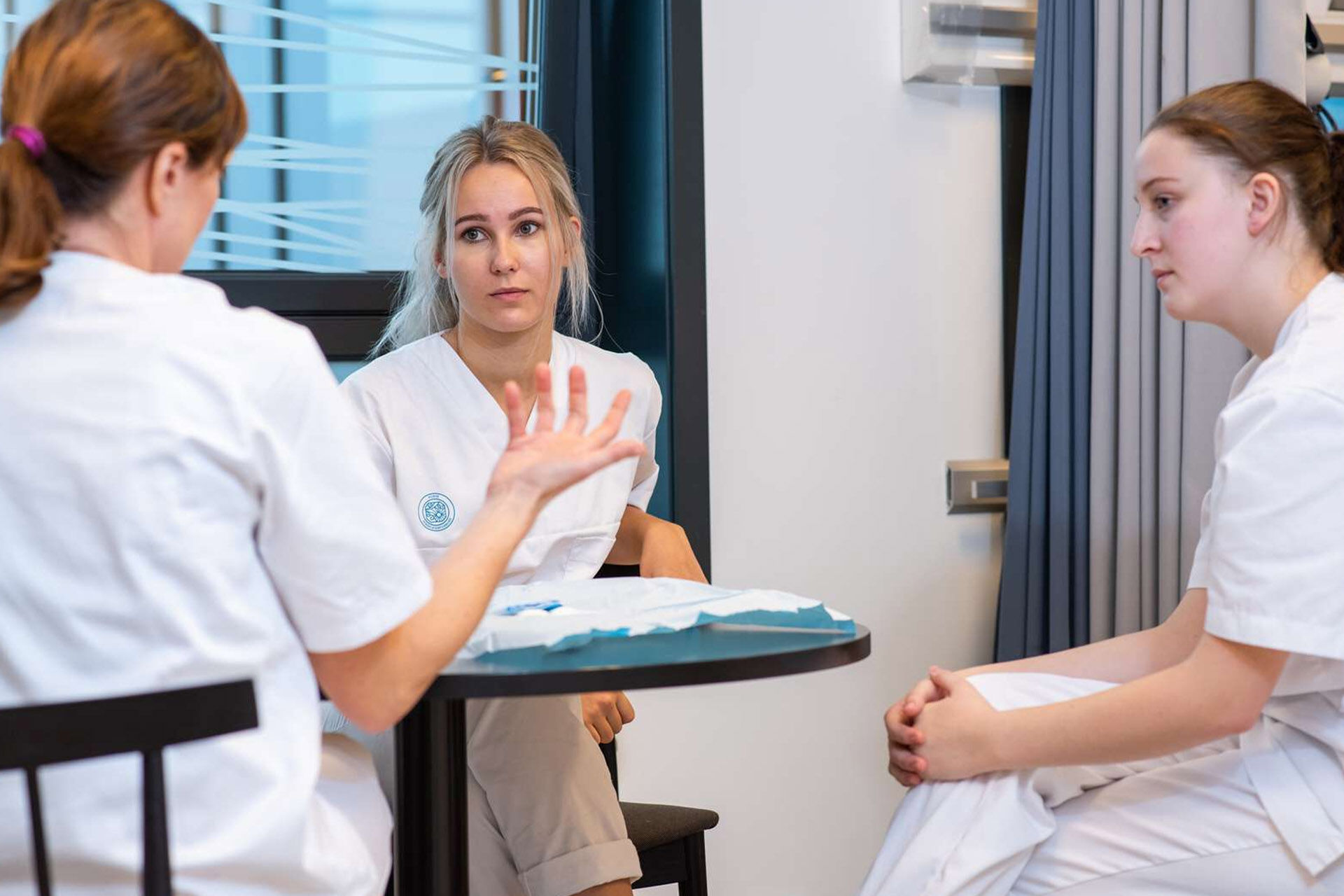 3 sykepleiere som sitter ved et bord og snakker sammen 