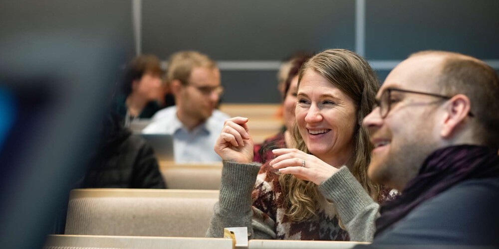 En smilende dame i samtale med en medstudent i forelesningssal