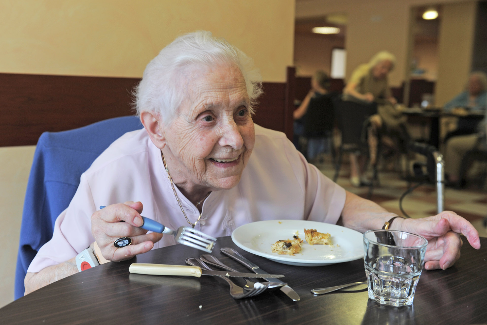En eldre kvinne sitter ved et bord og spiser