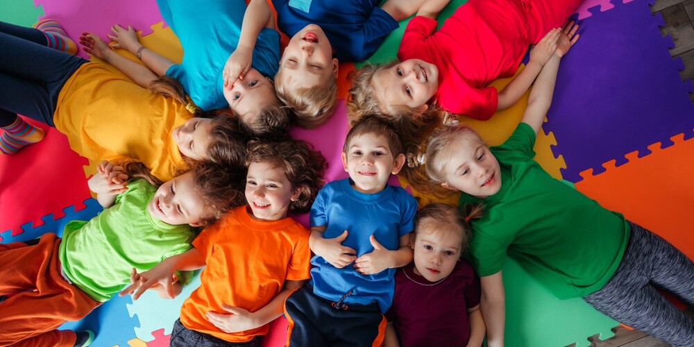 Barn med fargerike t-skjorter ligger i en sirkel og smiler til kamera