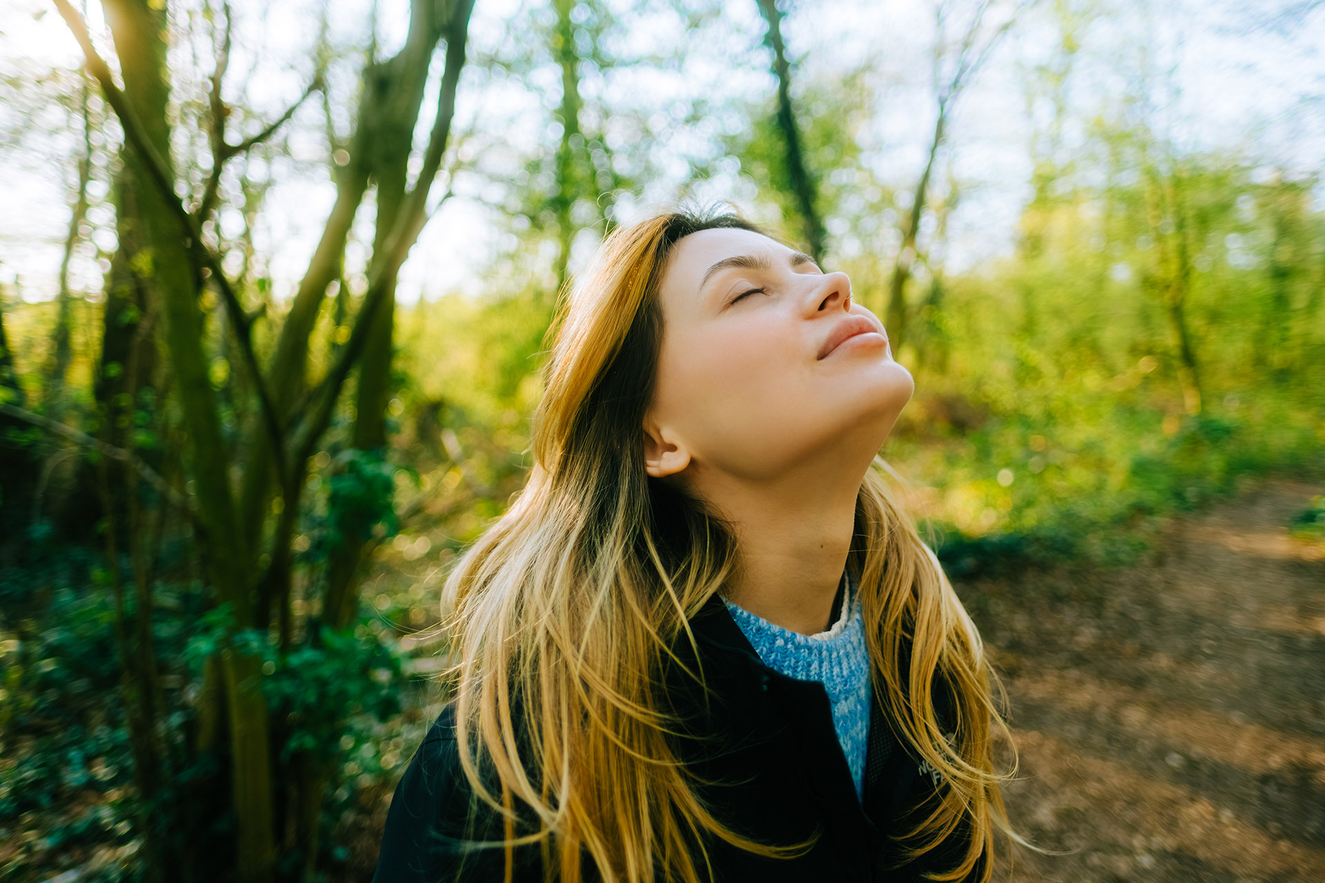 En ung kvinne med lukkede øyne som står i en skog og trekker inn frisk luft