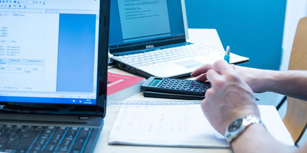 Et par hender som jobber med kalkulator, laptop og penn og papir
