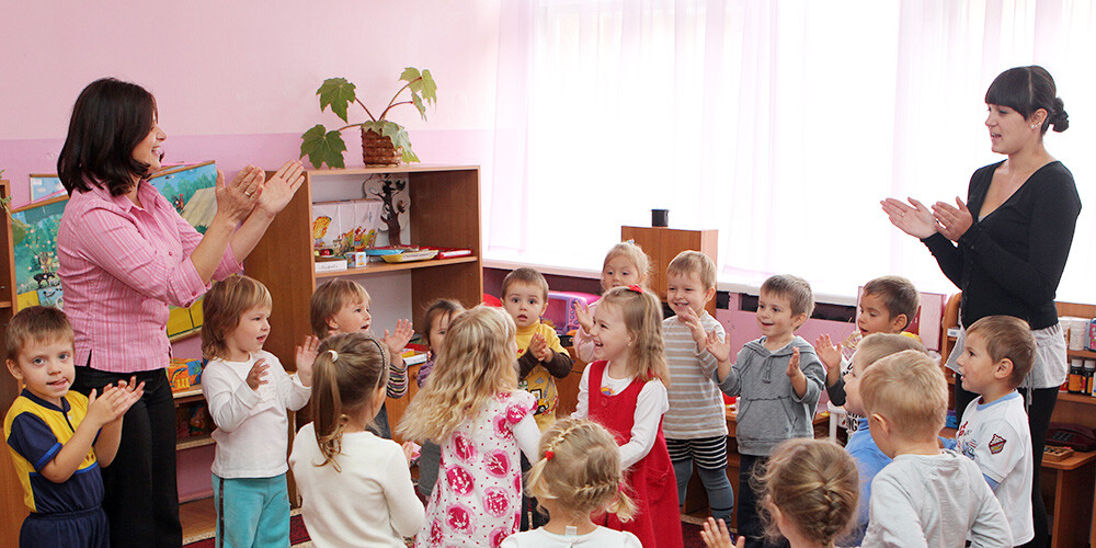 To barnehageansatte står sammen med en flokk med barn og alle klapper i hendene