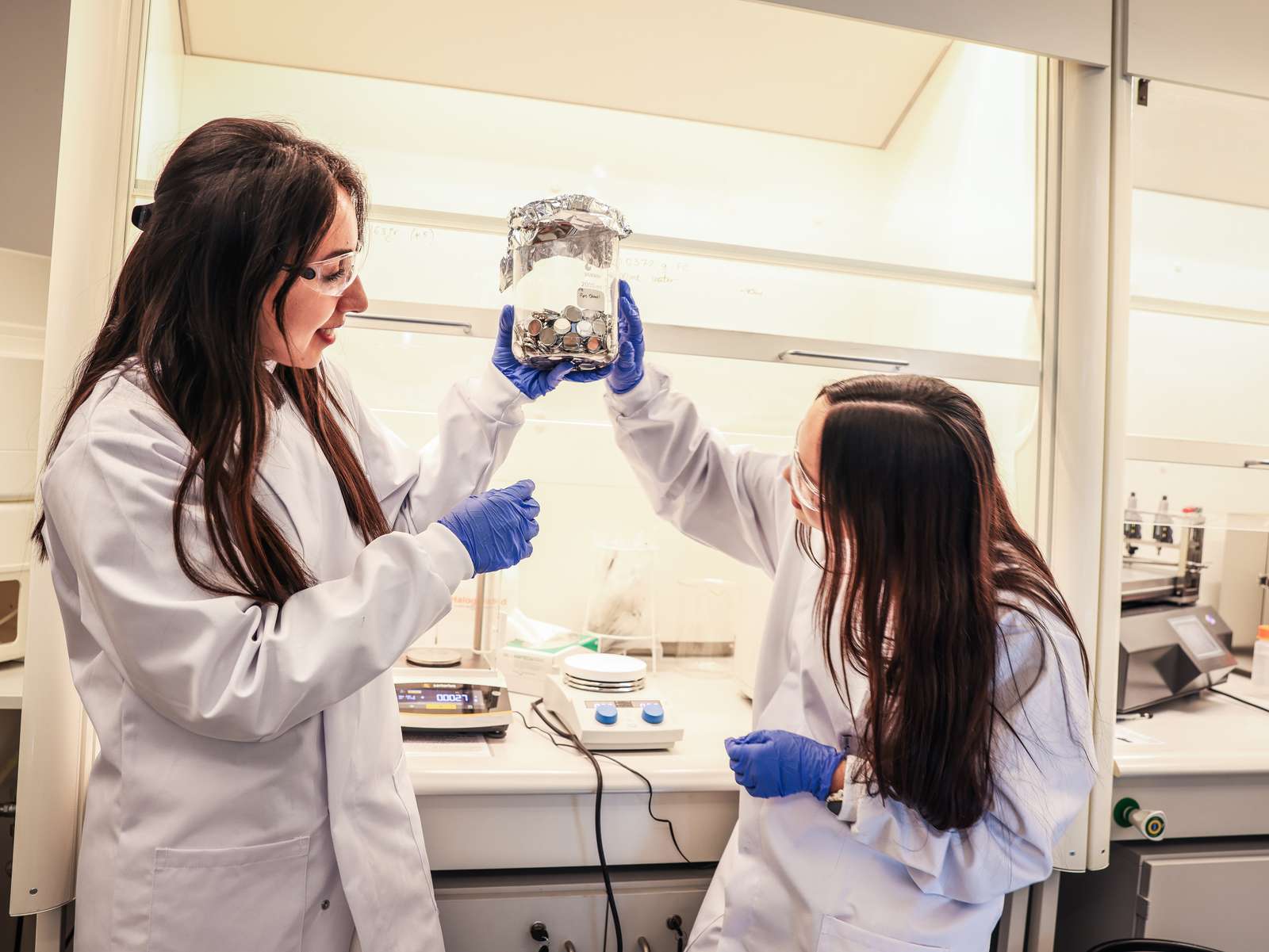 To jenter med vernebriller og forskerfrakker i en lab