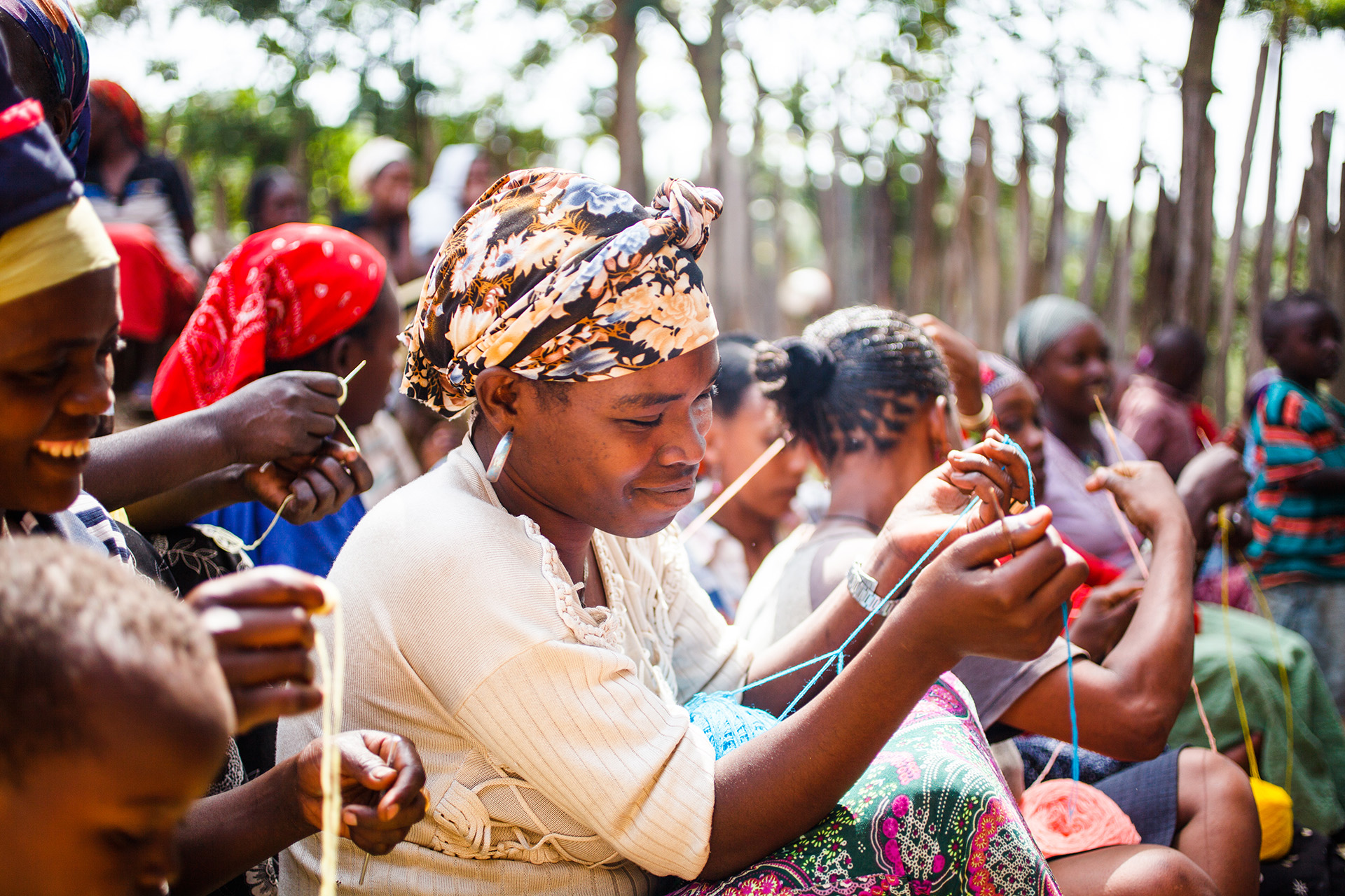 Afrikanske smilende kvinner sitter samlet og jobber med håndarbeid med garn i ulike farger.