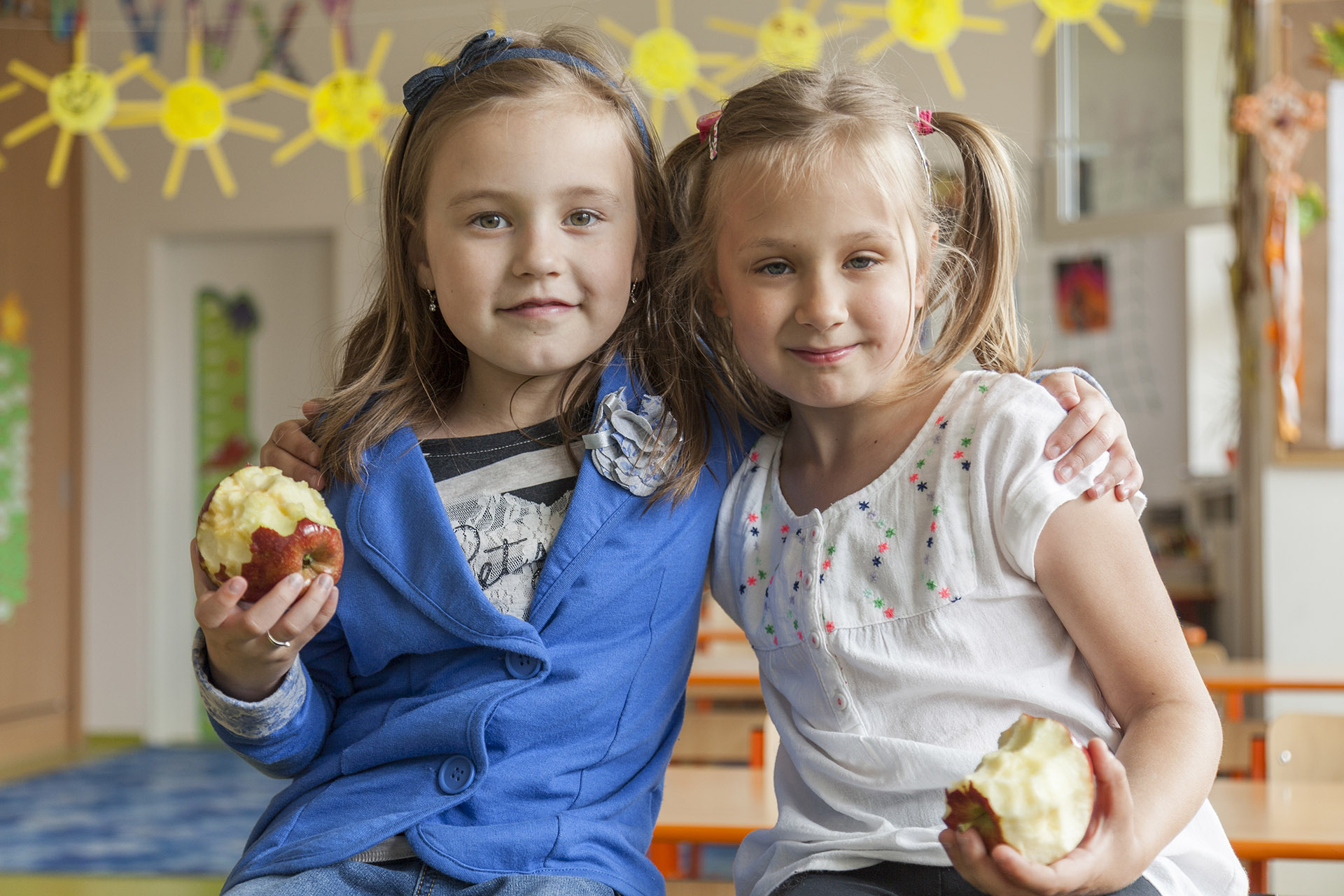 Foto av to unge jenter som holder rundt hverandre med hvert sitt eple i hånden
