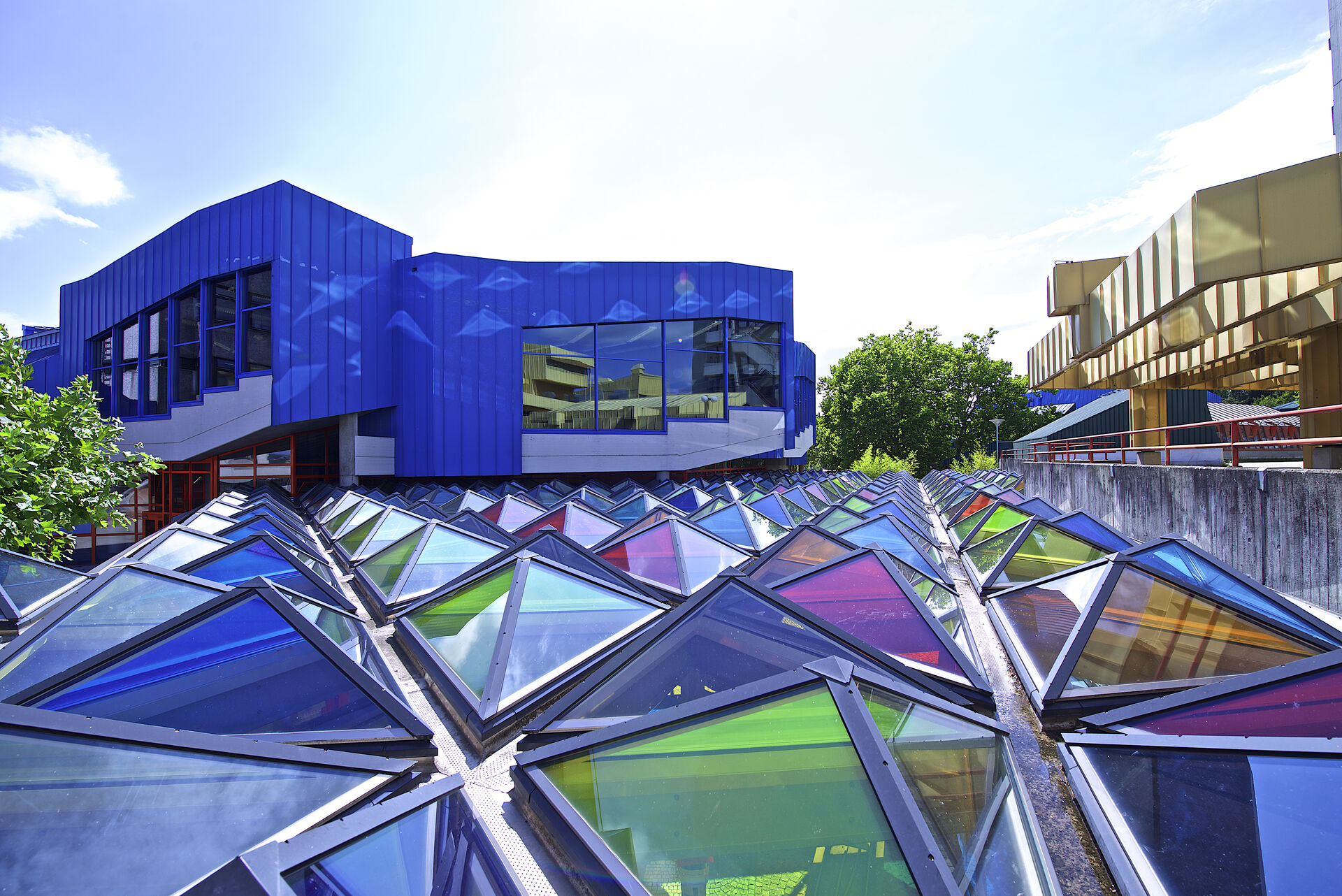 Utsiden av et av bygningene på campus der taket er laget av diverse trekanter av farget glass i forskjellige farger.