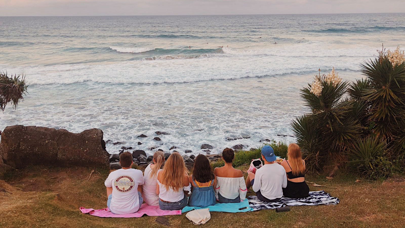 Syv ungde mennesker sitter på håndklær og ser ut over havet. Bildet er tatt på utveksling av en UiA-student.